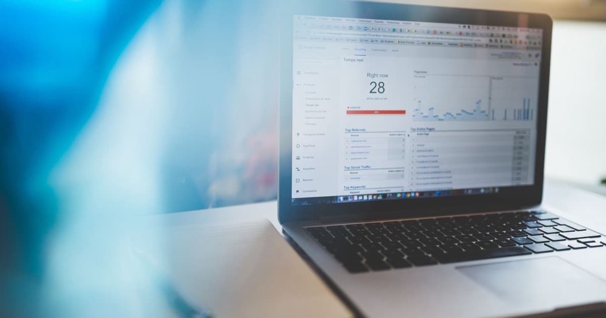 Laptop on a desk showing a Google Analytics dashboard beside a notebook and pen